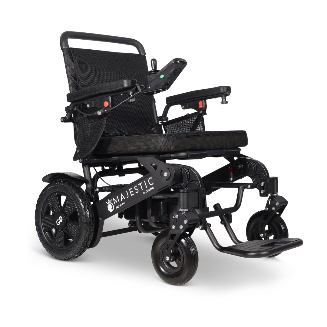 The ComfyGo Majestic 440 HD PLUS Bariatric Portable Powerchair is a black, travel-approved chair with a padded seat and backrest, armrests, right-arm control panel, large rear wheels, small front wheels, and "Majestic" branding on the side.